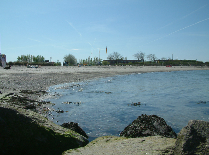 Der Sandstrand ist an der Wasserlinie mit ein paar Kieseln durchsetzt und durch kleine Felsmolen befestigt